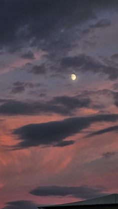 an airplane is flying in the sky at sunset with a full moon behind it and some clouds