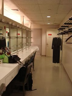 a long white counter in a room with lots of clothes hanging on the wall and some bags sitting on top of it