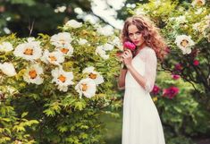 a beautiful young woman in a white dress holding a pink rose and looking at the camera