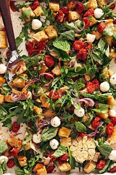 a salad with spinach, tomatoes, onions and croutons in a baking pan