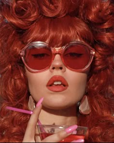 a woman with red hair and glasses holding a drink