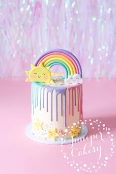 a cake with rainbow icing and stars on the top is sitting in front of a pink background