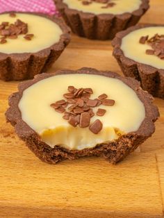 four desserts are sitting on a wooden table with white frosting and chocolate chips