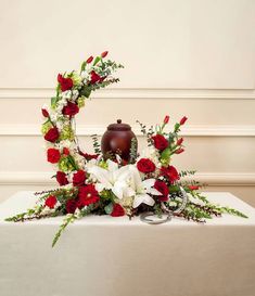 an arrangement of red and white flowers on a table with a vase in the middle