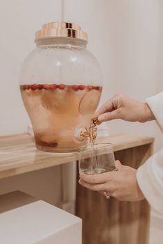 a woman is holding a glass in front of a vase