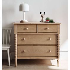 a wooden dresser sitting next to a white chair in a room with a lamp on top of it