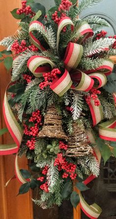 a christmas wreath hanging on the front door with red berries and evergreens around it