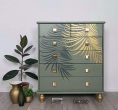 a green and gold chest of drawers next to a potted plant on the floor