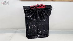 a black gift bag with red ribbon and splattered paint on it, sitting against a white wall