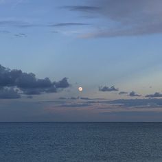 the moon is setting over the ocean with clouds in the sky and on the water