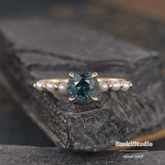 a ring with a green stone and pearls on it sitting on top of a rock