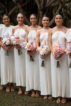 a group of women standing next to each other holding bouquets in their hands and wearing white dresses