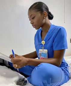 a woman in scrubs sitting on a bed with a clipboard and pen next to her