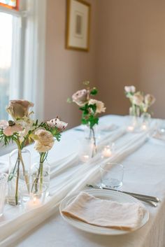 the table is set with white linens and glass vases filled with pink roses