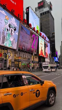 a yellow taxi cab driving down a street next to tall buildings with advertisements on them