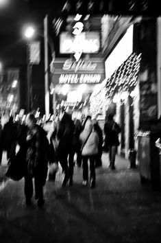 black and white photograph of people walking down the street at night with christmas lights in the background