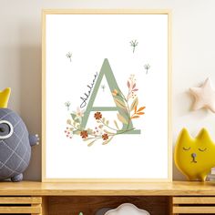 a poster with the letter a surrounded by flowers and leaves in front of a white wall