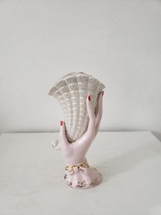 a white vase with a pink bird on it's head and hands holding an object