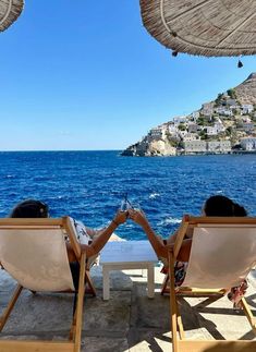 two people sitting in lawn chairs looking out at the ocean