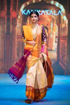 a woman walking down the runway in an orange and yellow sari with purple accents