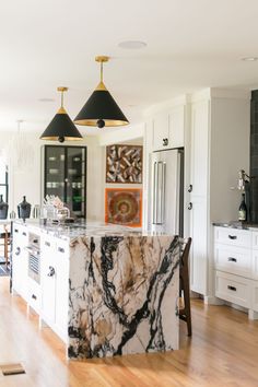 a marble island in the middle of a kitchen with two pendant lights hanging over it