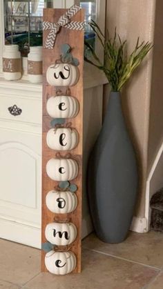 a wooden sign that has pumpkins on it next to a vase with some plants in it