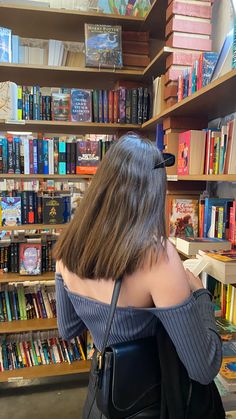 a woman with long hair is looking at books in a book store and she has her back to the camera