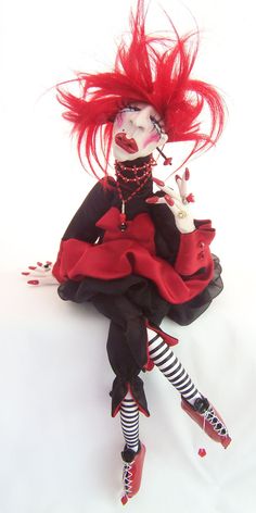 a doll with red hair and makeup is sitting on a white background wearing black and red clothes