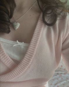 a woman wearing a pink sweater with a heart pendant on her neck and a white bow tie