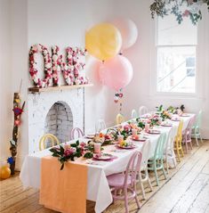 a table set up for a party with pink, yellow and green balloons hanging from the ceiling