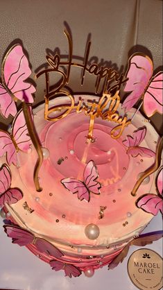 a pink cake with butterflies on it and the words happy birthday written in gold letters