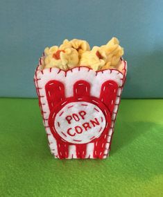 a small red and white popcorn box with pop corn in it on a green surface