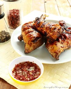 two white plates topped with chicken wings next to a bowl of chili and seasoning