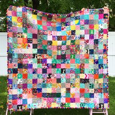 a colorful quilt is hanging on a clothes rack in the grass near a white fence