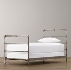 a metal bed frame with white sheets and pillows on top of wooden floor next to gray wall