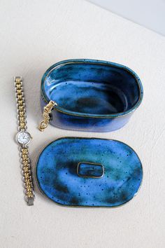 two pieces of blue pottery sitting on top of a white table next to a watch