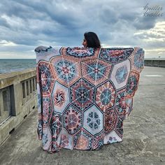 a woman is standing on the beach with a blanket over her head and looking out at the ocean