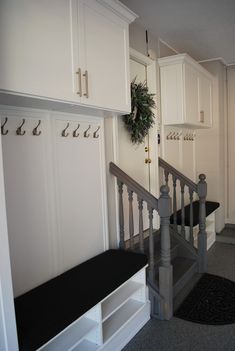 a hallway with white cabinets and black bench next to it's coat rack on the wall