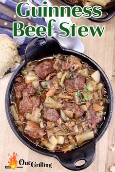 a skillet filled with beef and potatoes on top of a wooden table next to bread