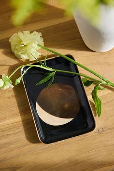 a vase with flowers on a table next to a cell phone that has been placed on it