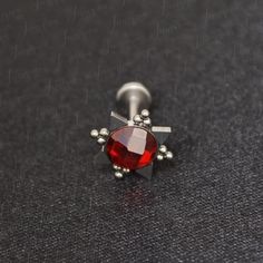 a pair of piercings with an oval shaped red stone in the center on a black surface