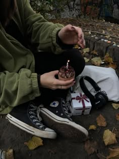 a woman sitting on the ground holding a small cake with a candle in her hand