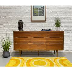 a wooden dresser sitting in front of a white brick wall next to potted plants