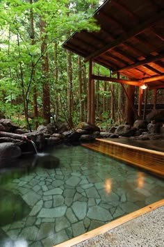 an outdoor hot tub in the middle of a forest with rocks and trees around it