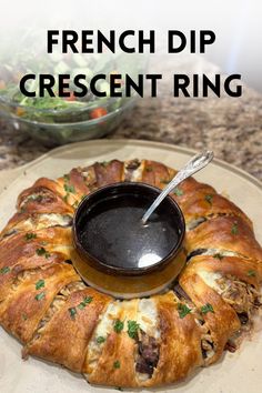 a croissant ring is on a plate with a bowl of dipping sauce in it