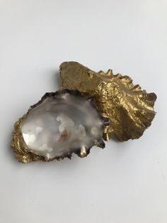 two pieces of gold leaf and an oyster shell on a white surface with no background