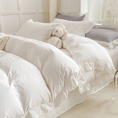 a teddy bear sitting on top of a bed with white sheets and pillows in front of a window