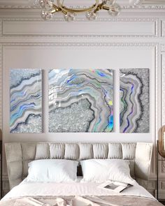 three paintings on the wall above a bed in a room with white furniture and chandelier