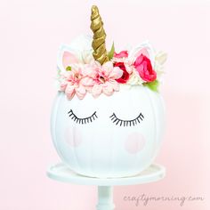 a white pumpkin decorated with pink flowers and a unicorn's horn on top is sitting on a pedestal