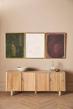 three paintings hang on the wall next to a wooden cabinet with two bowls in it